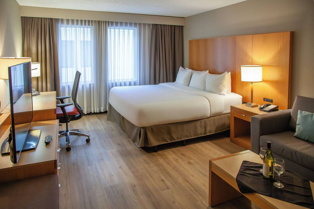 A hotel room with a large bed, a desk with a computer, a chair, a sofa, and a lamp.