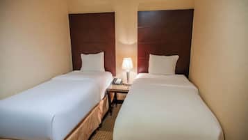 A hotel room with two single beds, a nightstand with a lamp, and a telephone.