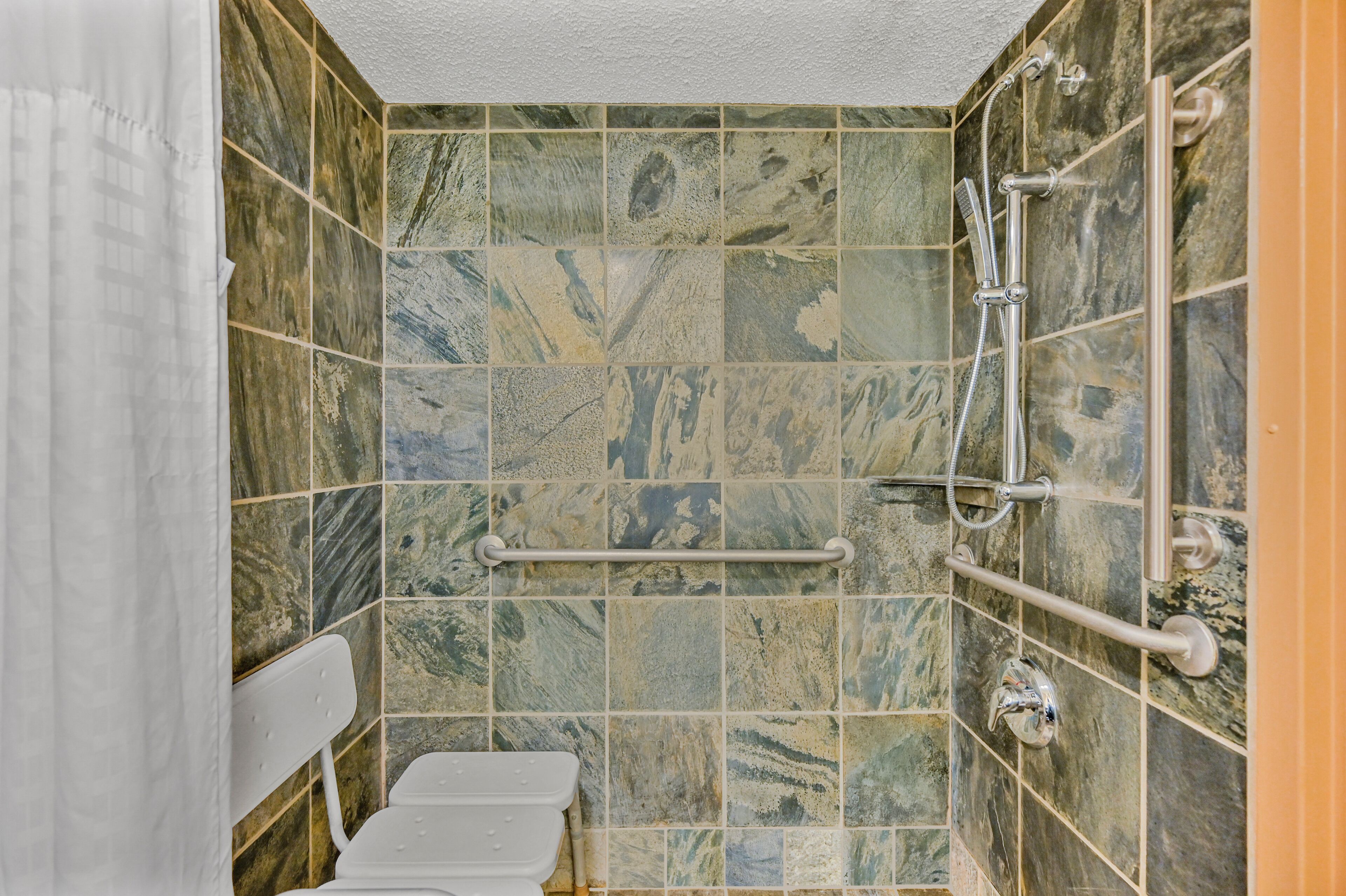Un baño con inodoro, ducha con cabezal de ducha de mano y barra de apoyo.