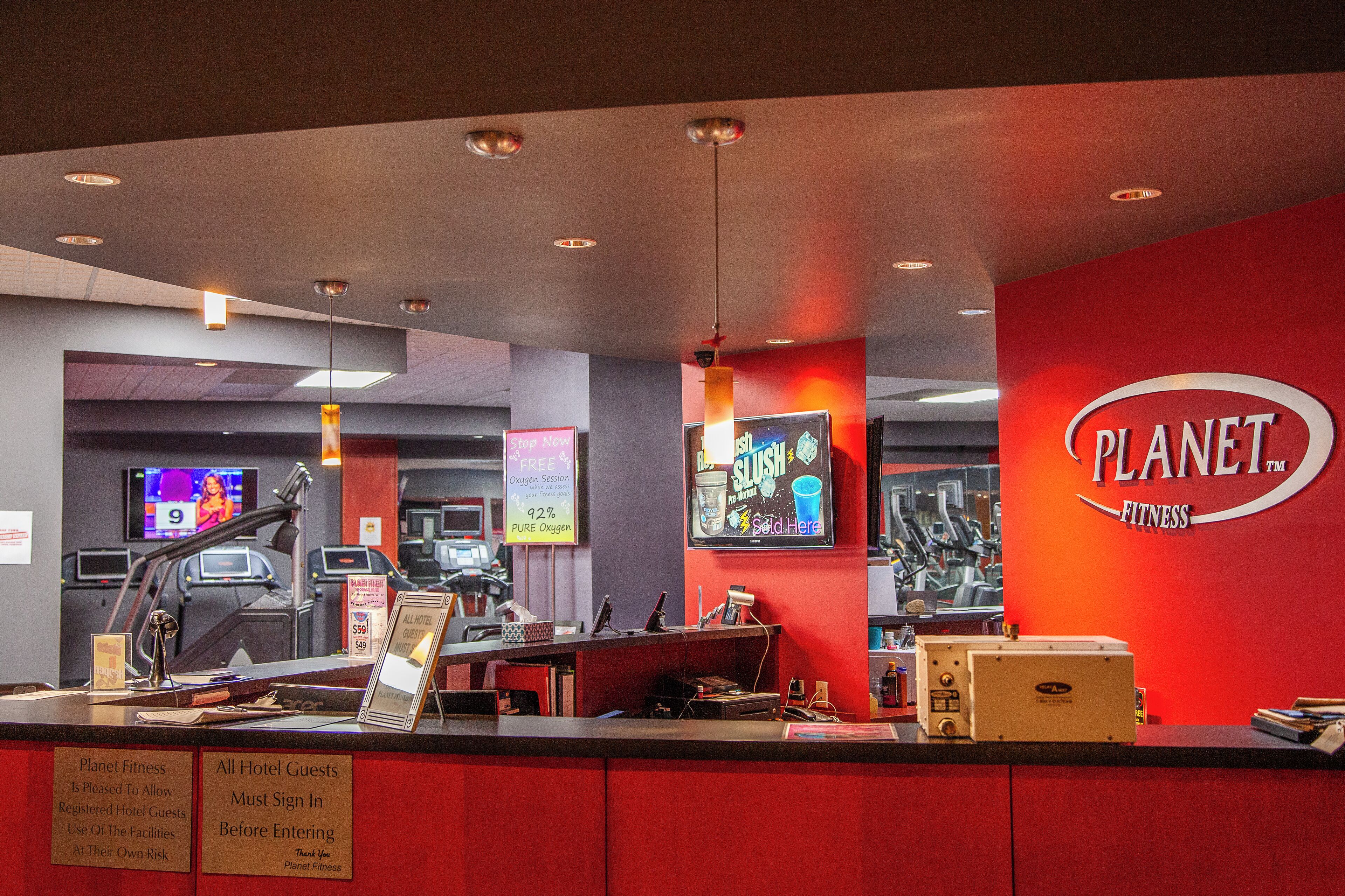 A Planet Fitness facility with a reception desk, exercise equipment, and a red wall with the Planet Fitness logo.