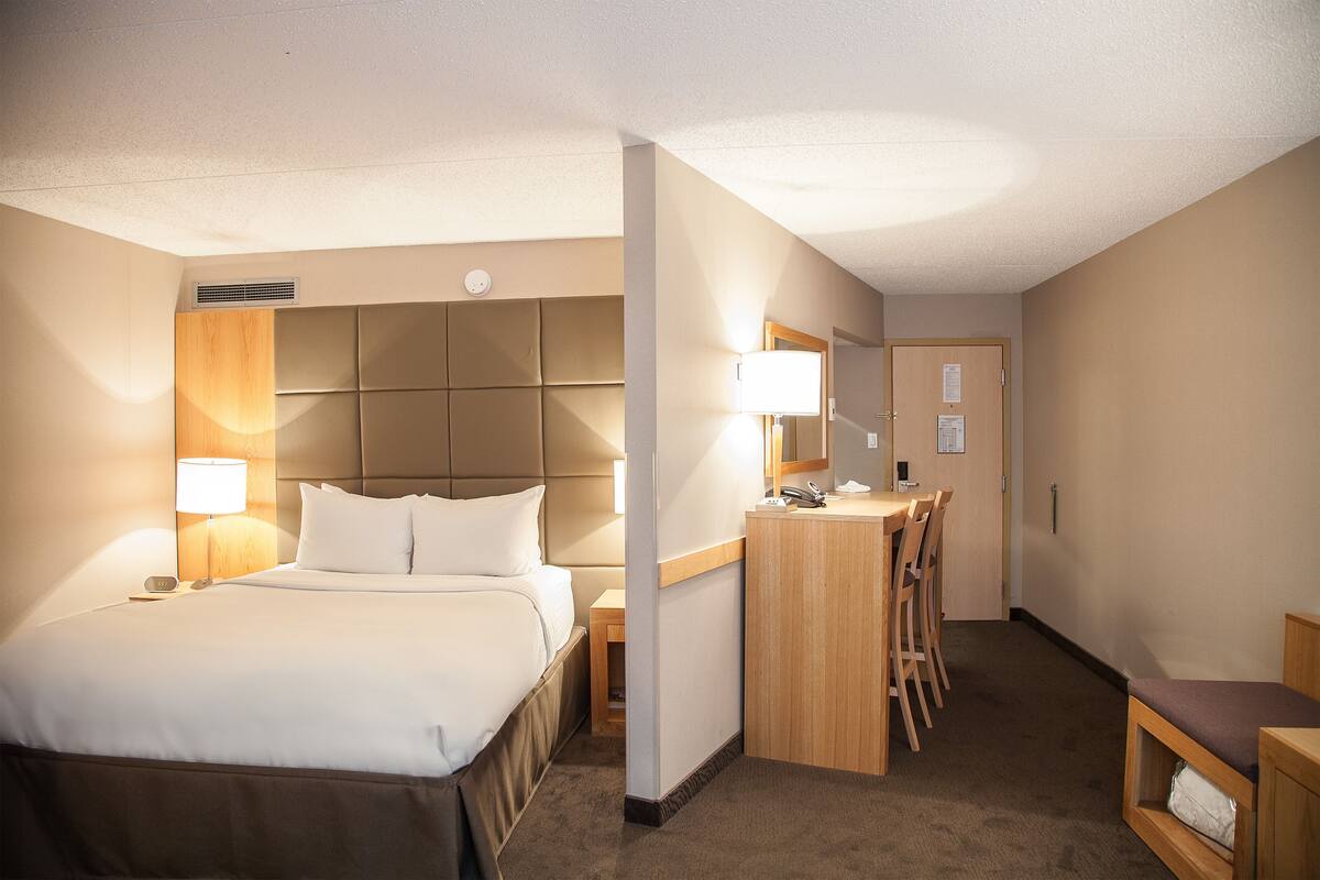 A hotel room with a large bed, bedside lamps, a desk with chairs, and a small seating area.