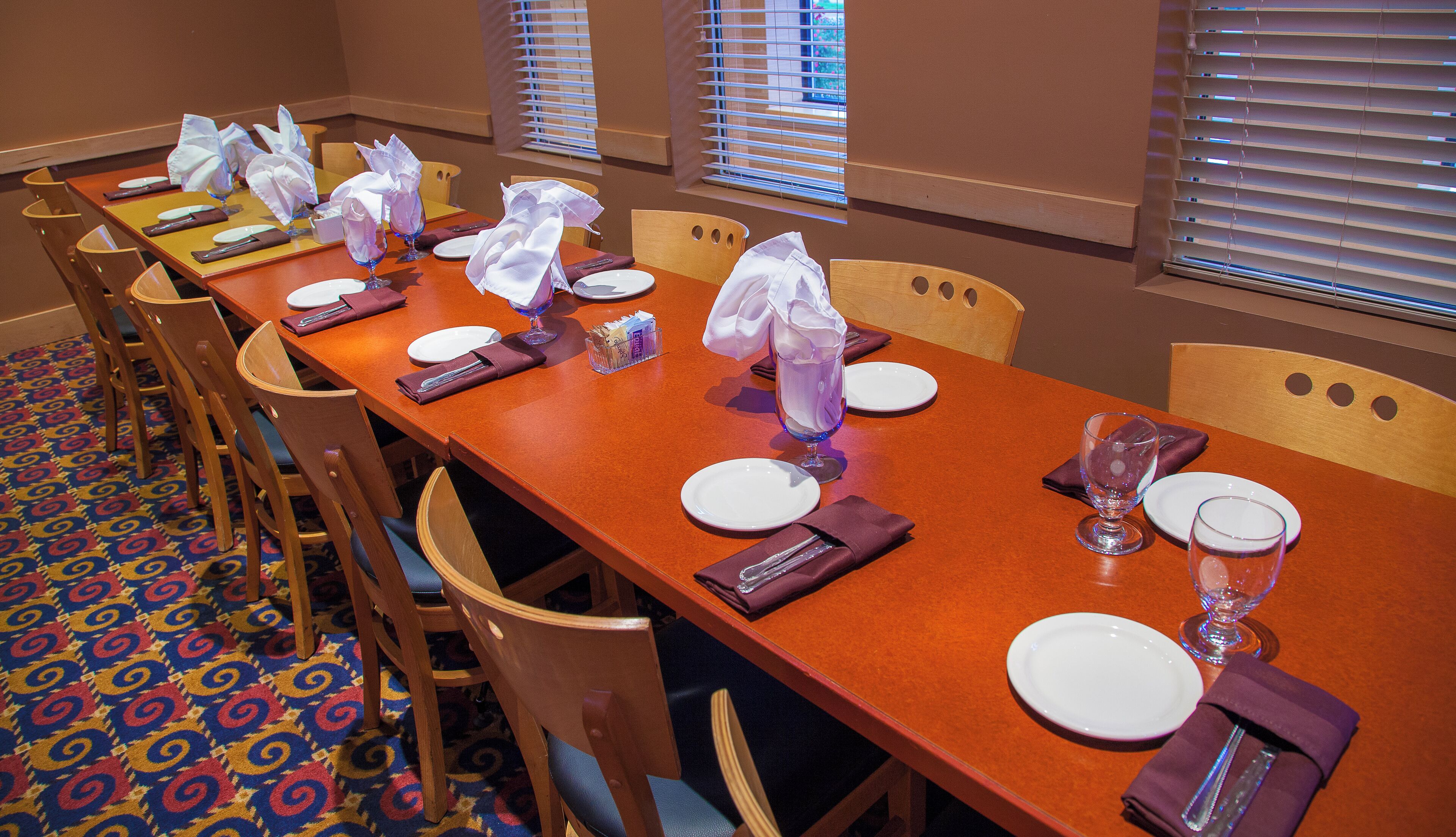 A dining area with a long table set for multiple guests, chairs, and a patterned carpet.