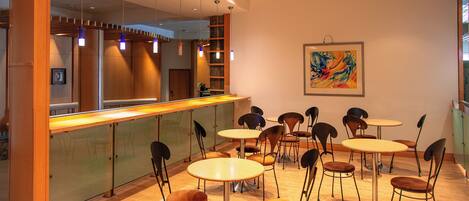 A restaurant with round tables and chairs, a counter, and a painting on the wall.