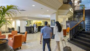 A hotel lobby with a reception desk, seating area, and a staircase.