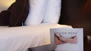 Una cama con ropa blanca y una carta de almohadas sobre la mesita de noche.