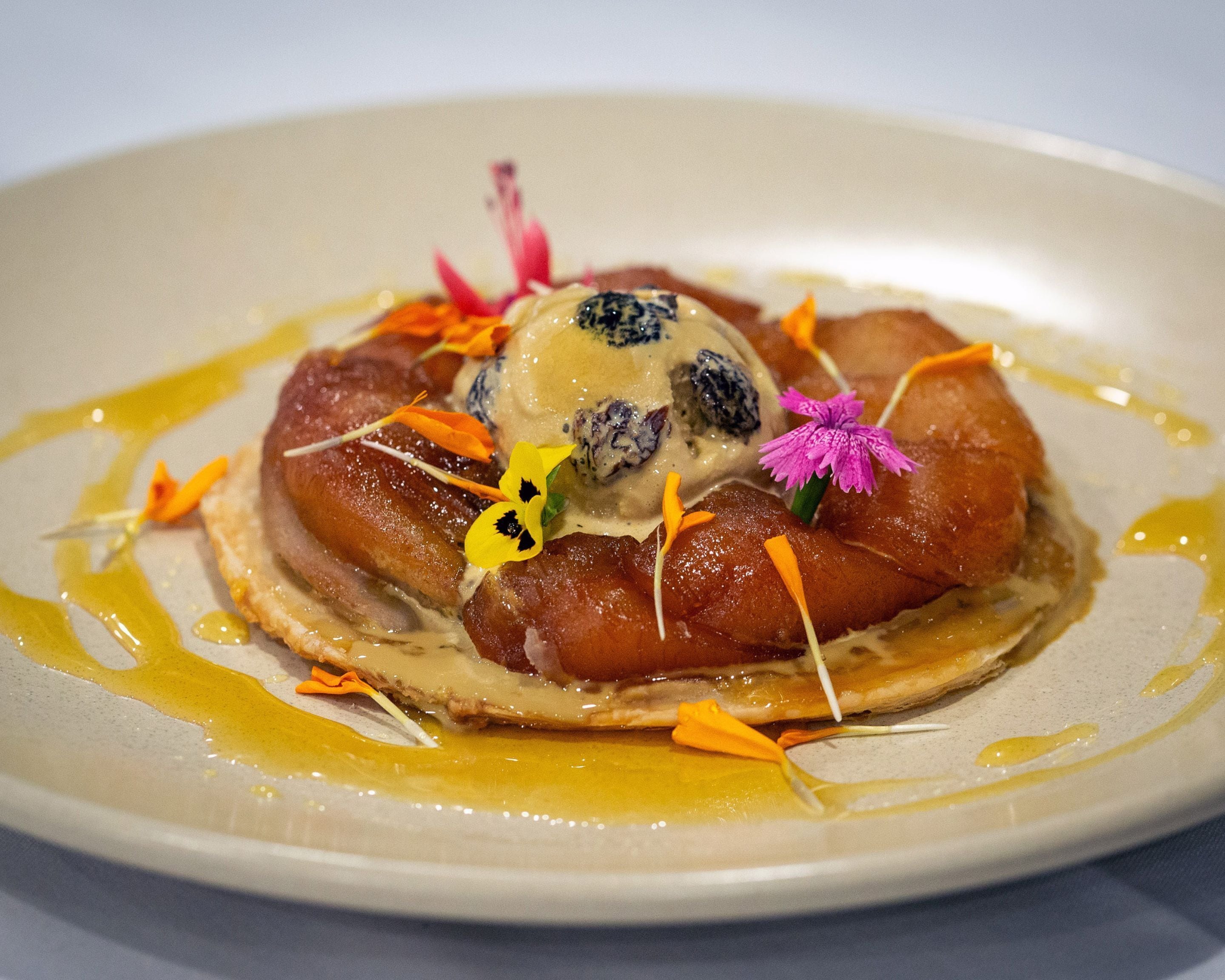 Un dessert surmonté d’une crème onctueuse, décoré de fleurs et nappé d’une sauce jaune.