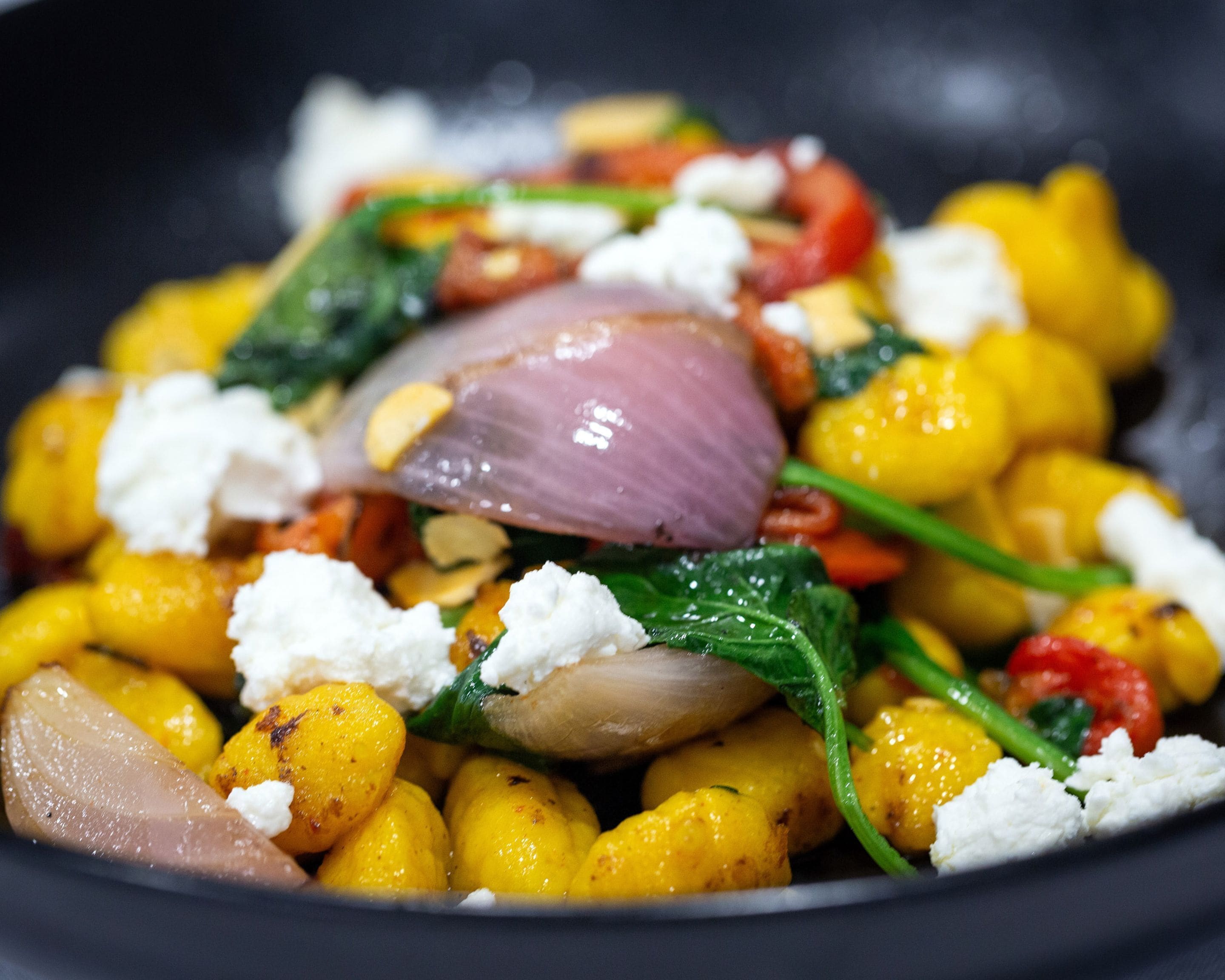 A close-up of a colorful dish with yellow squash, red onion, and white cheese.