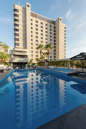 Un hotel con piscina, palmeras y un edificio grande al fondo.