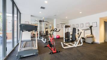 A gym with cardio machines, weight training equipment, and a large mirror.