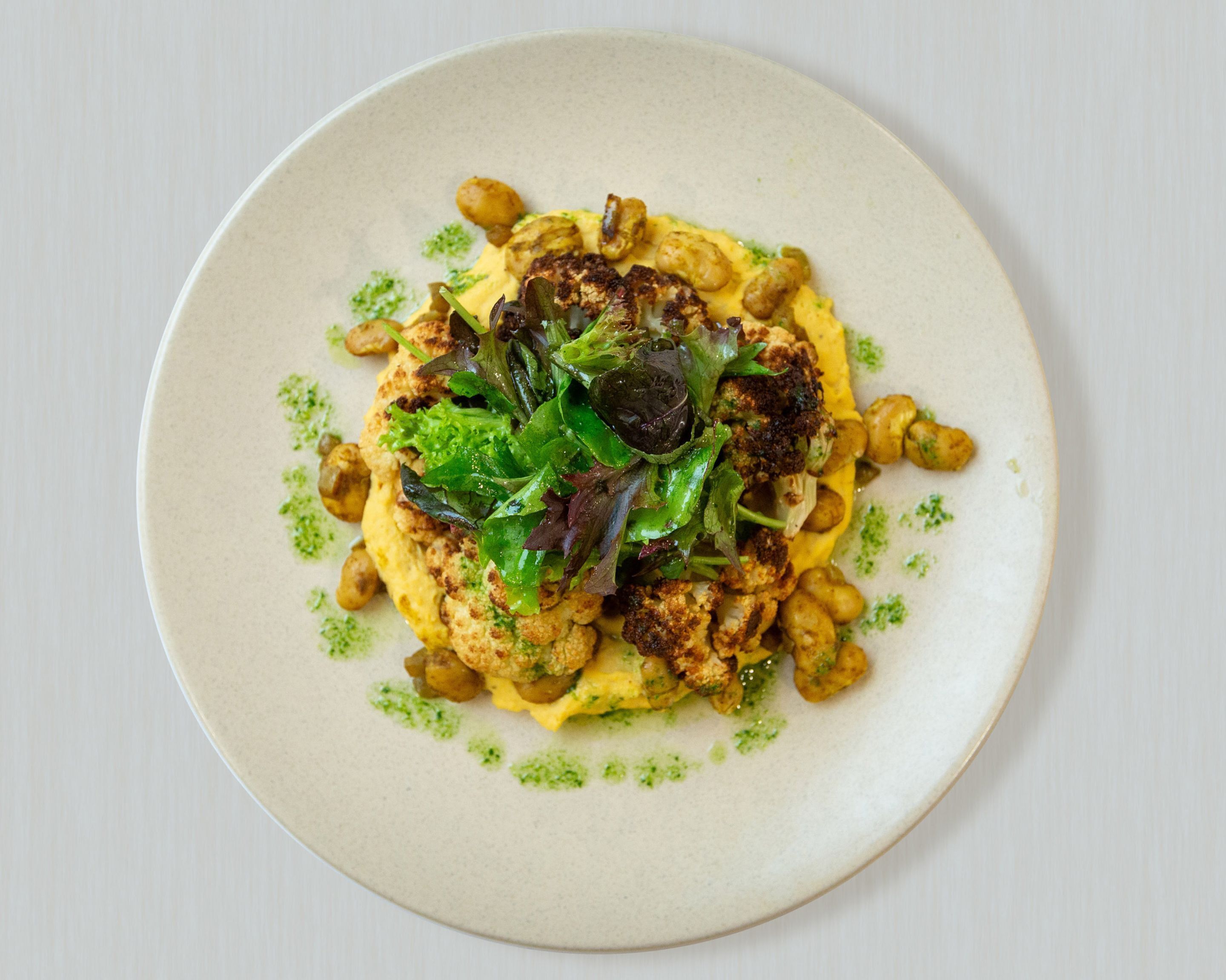 A plate of food with a creamy base, topped with greens, nuts, and chickpeas.