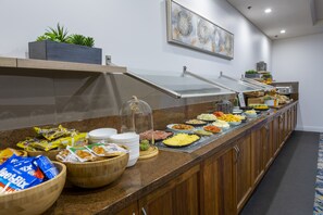Disposición de bufé con diversos alimentos y una planta decorativa sobre una encimera de madera.