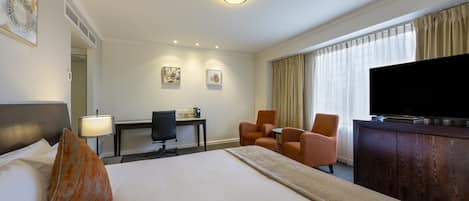 A hotel room with a large bed, a desk with a chair, a television, and a window with curtains.
