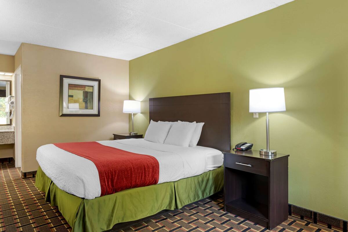 Una camera d'albergo con un letto, due lampade ai comodini, un tavolino con il telefono e un quadro appeso alla parete.