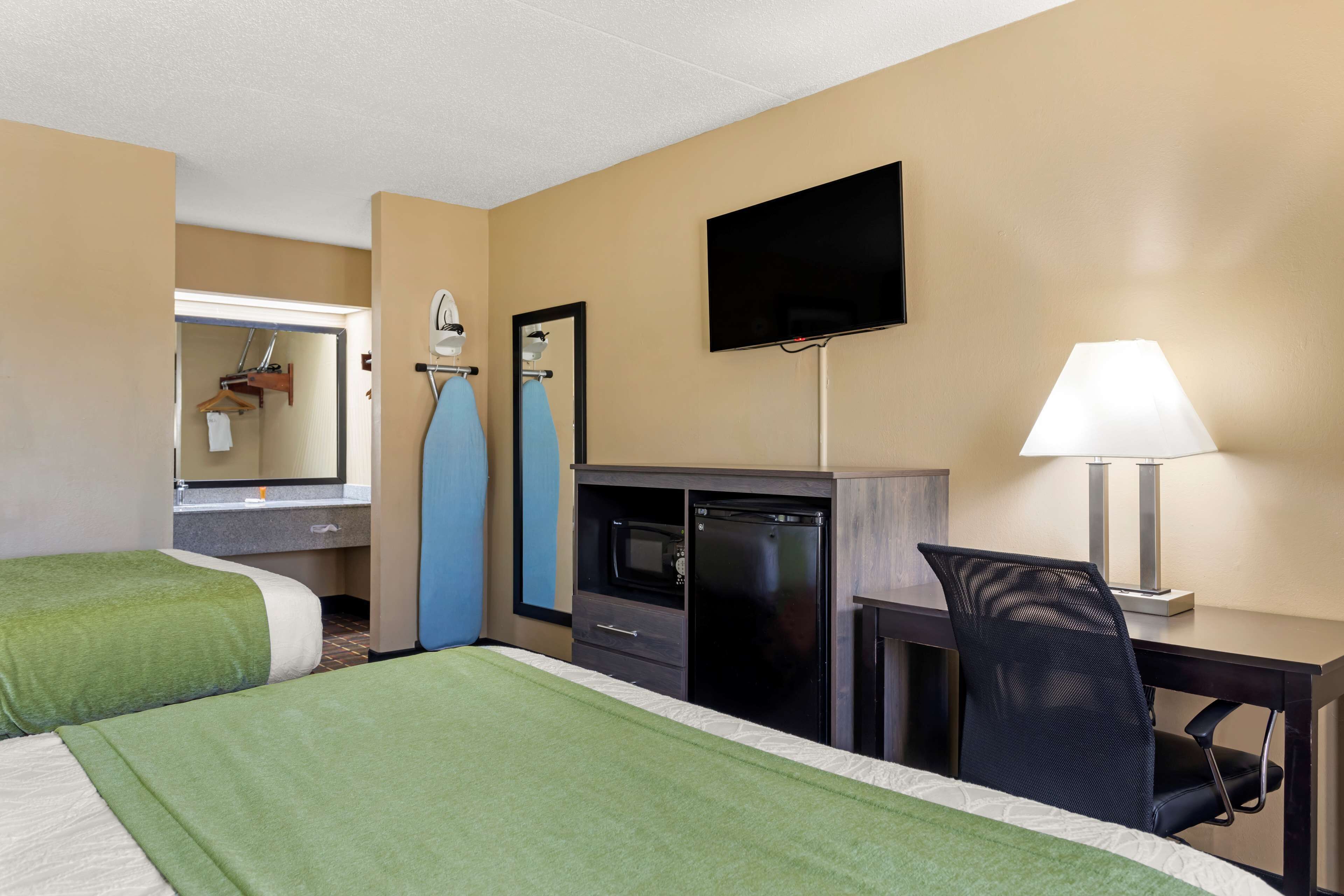 A hotel room with two beds, a desk with a chair, a television, a microwave, and a mirror.
