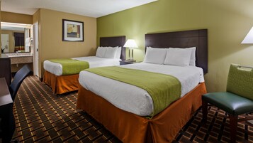 Una habitación de hotel con dos camas, un escritorio, una silla, un espejo y una lámpara.