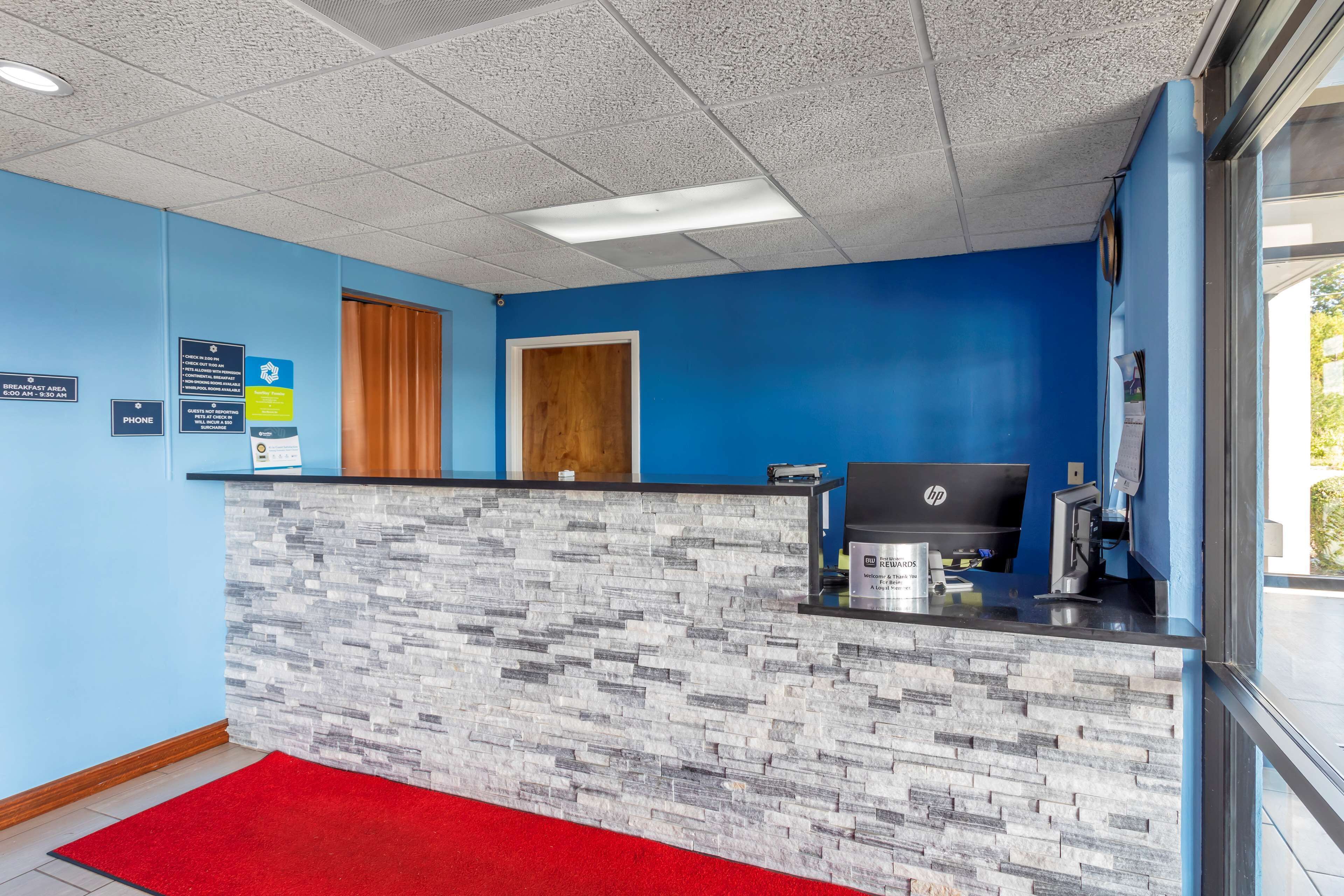A reception area with a stone counter, a red carpet, a wooden door, and a HP computer.
