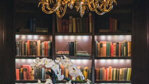 A library with bookshelves, a chandelier, and a table with flowers and candles. - The Goodwin Hotel (Hartford)