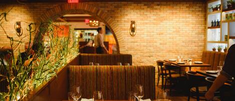 A restaurant interior with brick walls, wooden tables, and cushioned booths.
