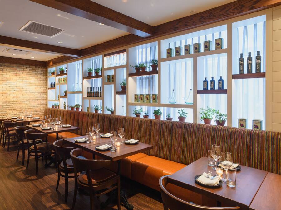 A restaurant with wooden tables and benches, potted plants on shelves, and a brick wall.