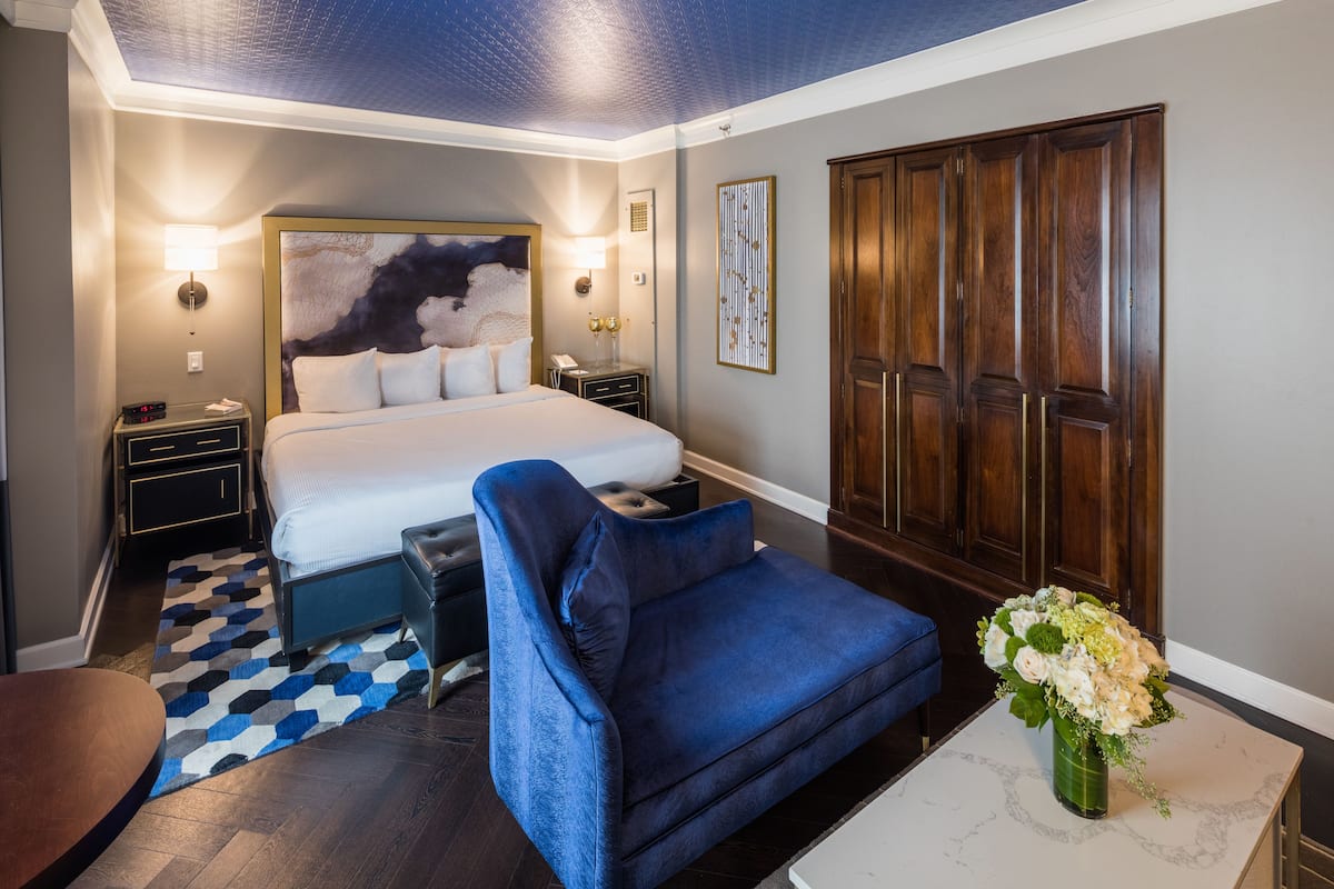A hotel room with a bed, a blue sofa, a desk, a wardrobe, and a patterned rug.