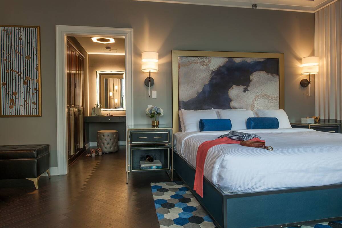 A modern hotel room with a large bed, a vanity with a mirror, and a hallway leading to a bathroom.