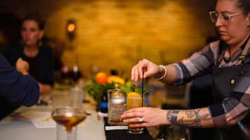 A bartender preparing a drink at a bar with a brick wall background.