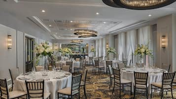 A hotel dining area with round tables, chairs, and chandeliers.