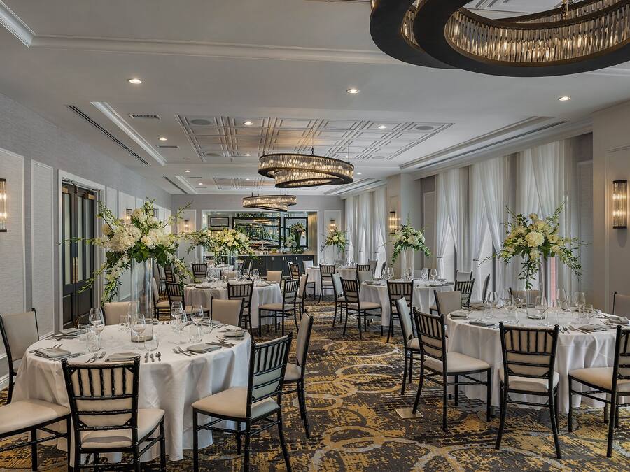 A hotel dining area with round tables, chairs, and chandeliers.
