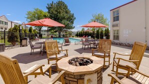 An outdoor seating area with wooden chairs and tables, a fire pit, and red umbrellas. - Best Western Plus Loveland Inn (Loveland)