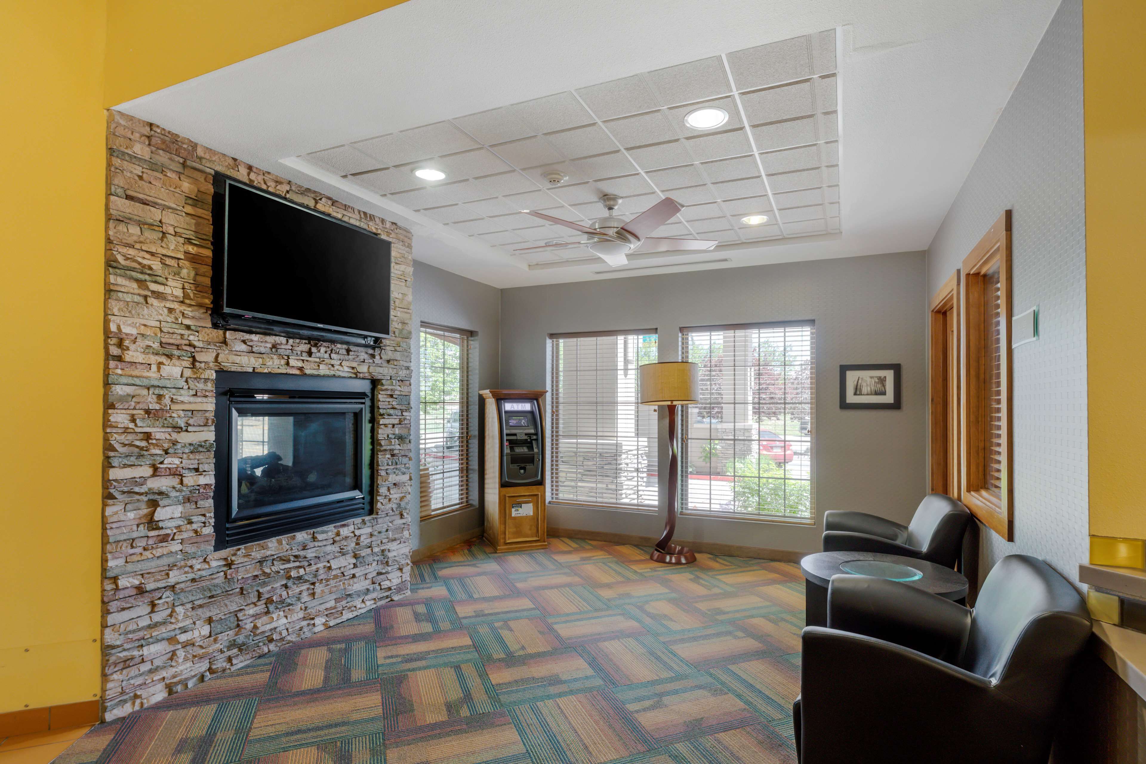 A room with a stone wall, a flat-screen TV, a ceiling fan, a vending machine, and a seating area with chairs and a table.