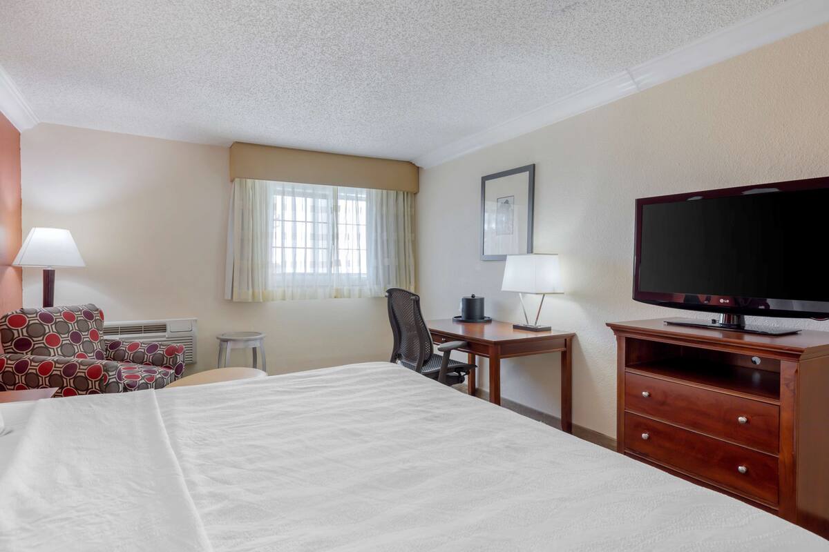 A hotel room with a large bed, a desk with a television, a chair, and a small table.