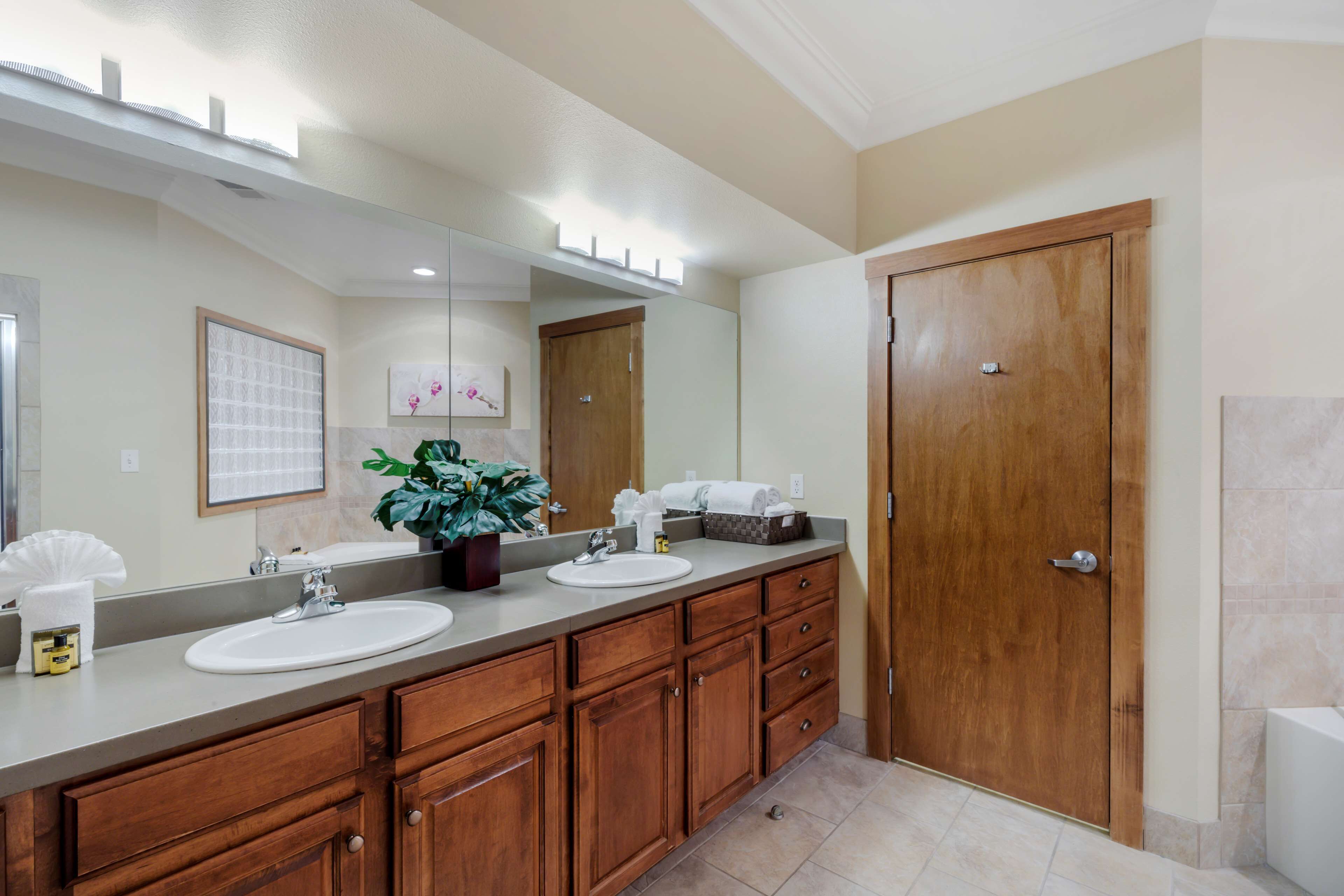 A bathroom with a large mirror, wooden cabinets, a sink, and a door.