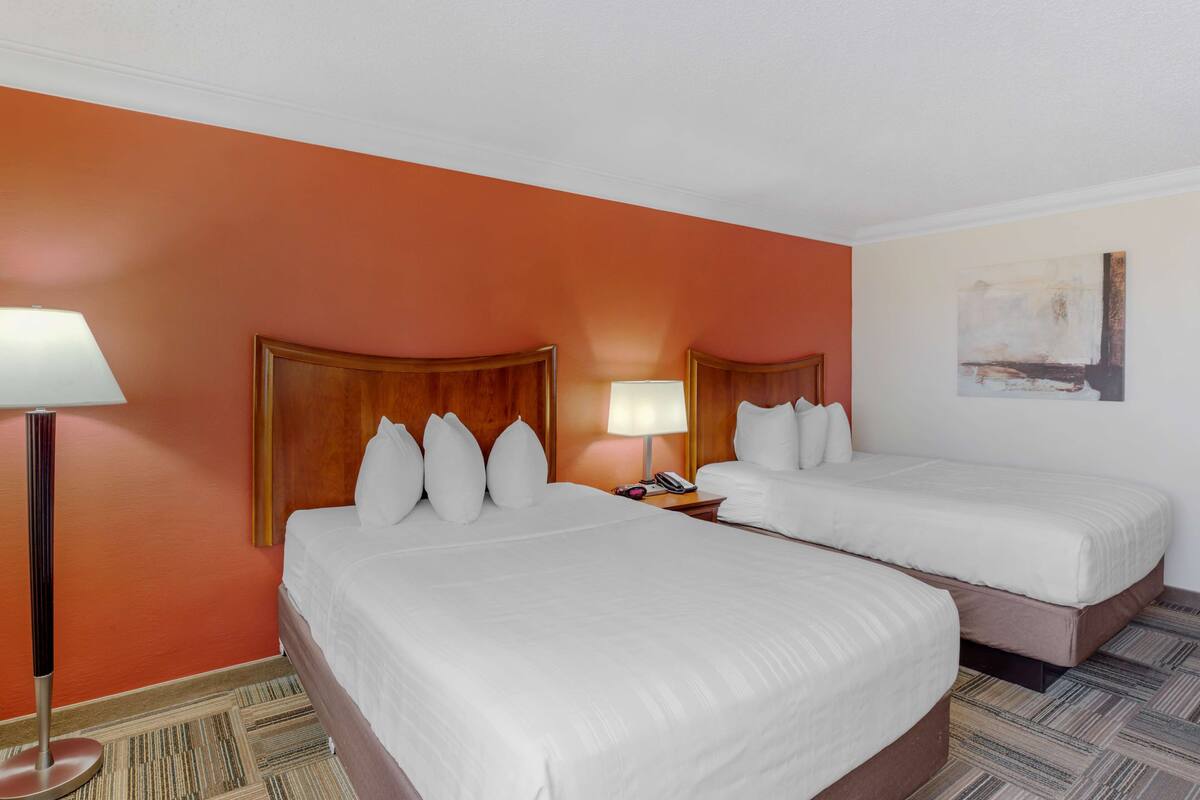 A hotel room with two beds, a nightstand with a lamp, and a painting on the wall.