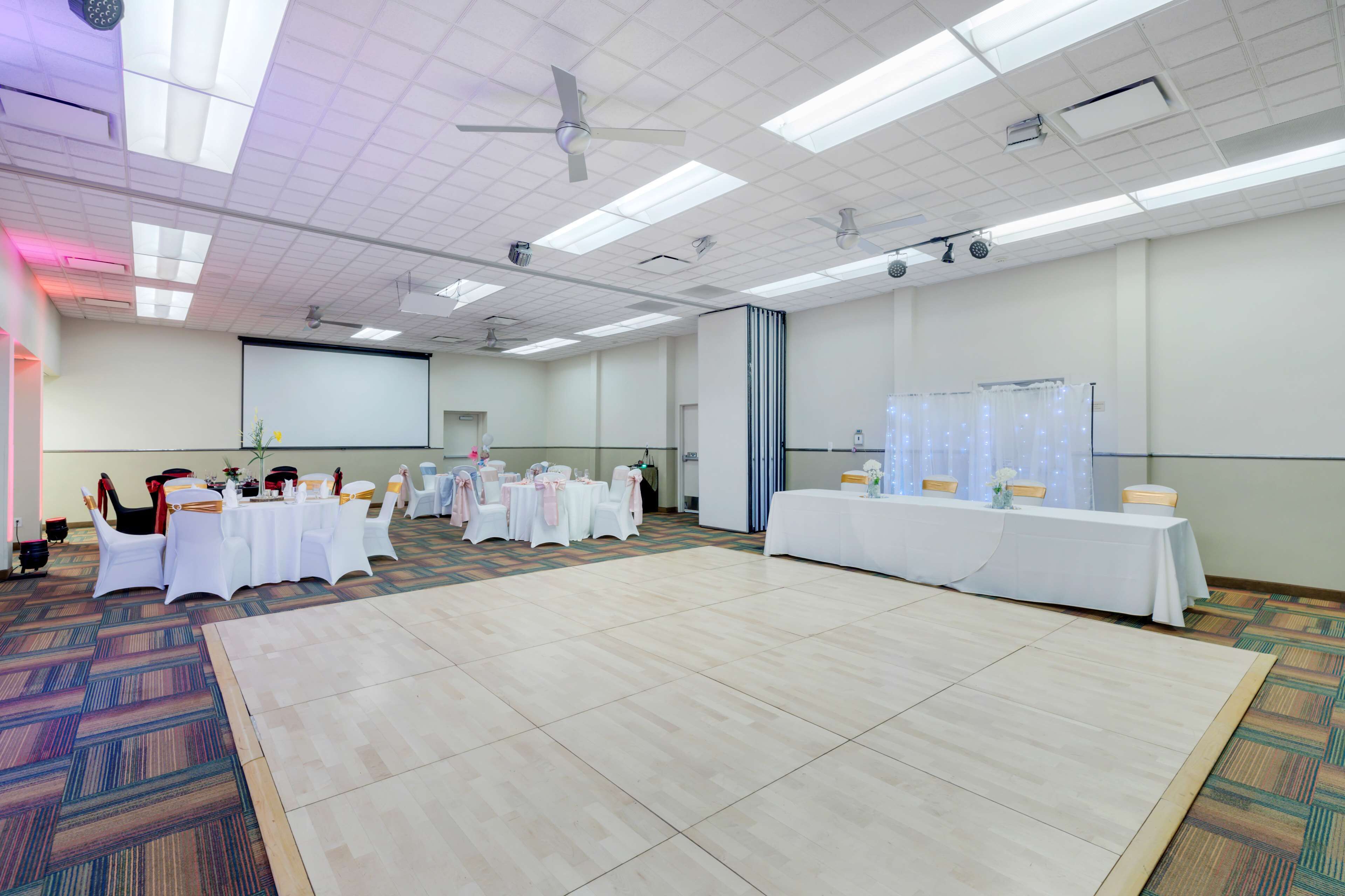 A large conference room with a stage, multiple tables with chairs, and a projector screen.
