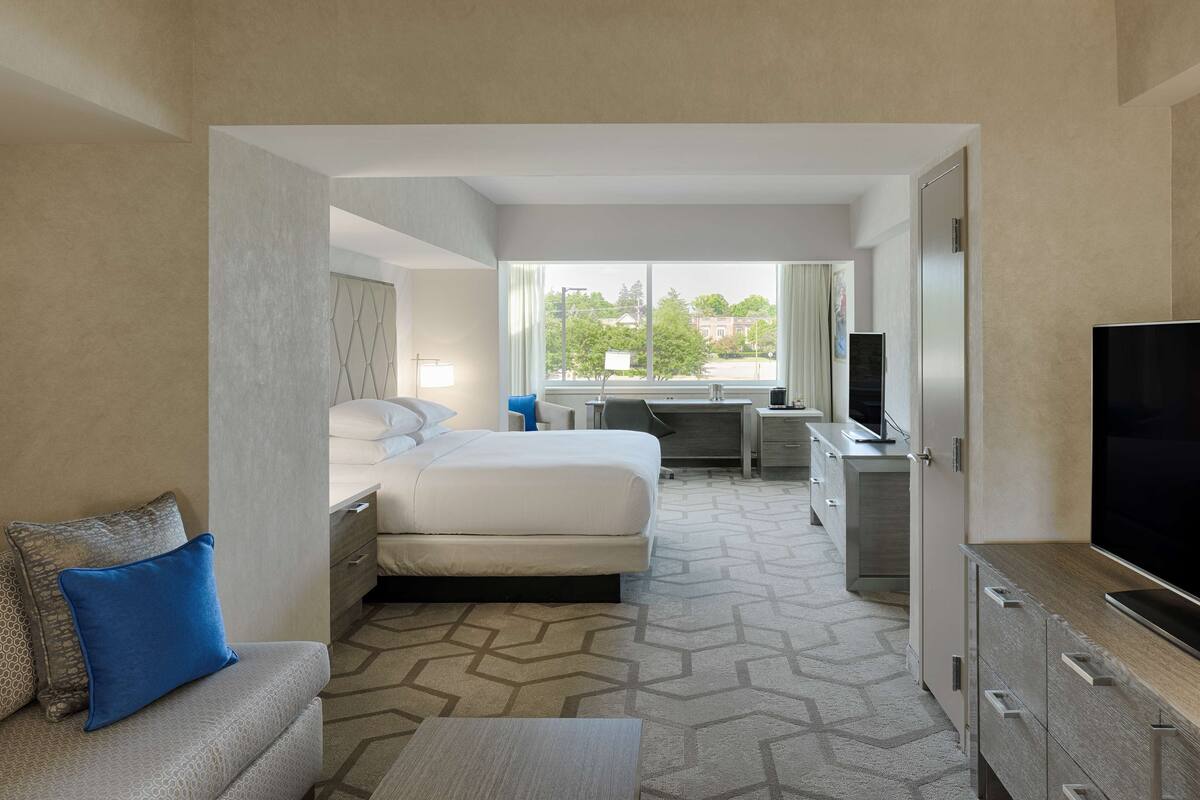 A hotel room with a bed, a desk, a television, and a view of the outdoors.