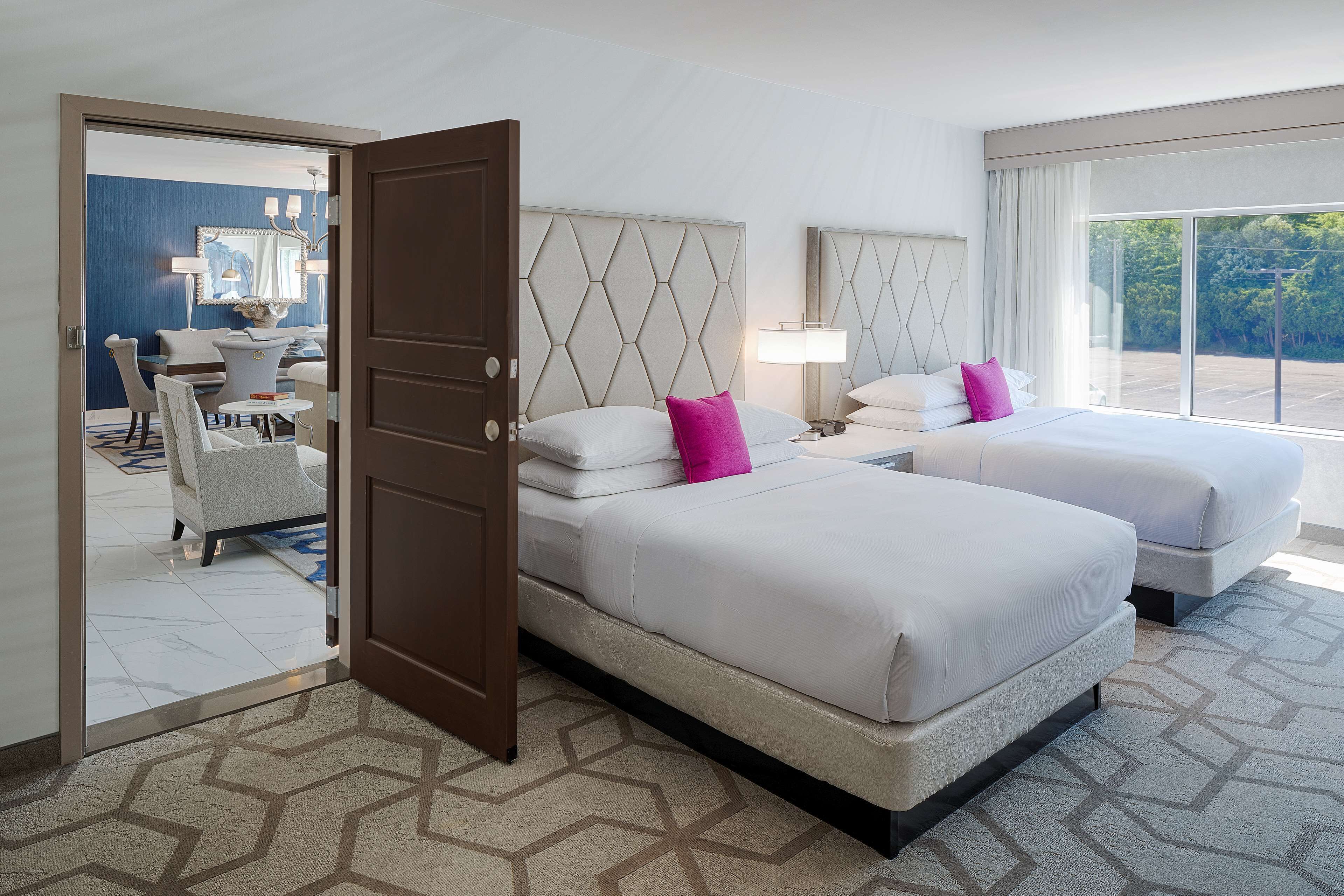 A hotel room with two beds, a large window, and a view of the outdoors.