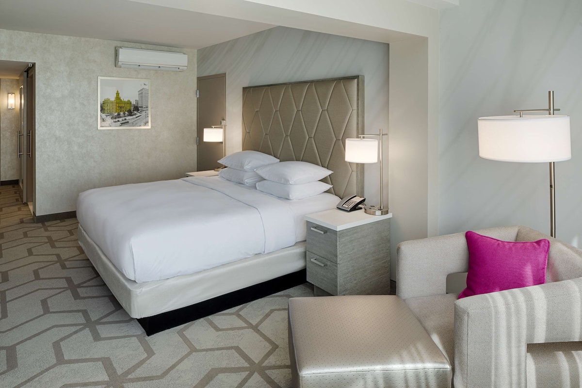 A hotel room with a large bed, a nightstand with a phone, a chair, and a lamp.
