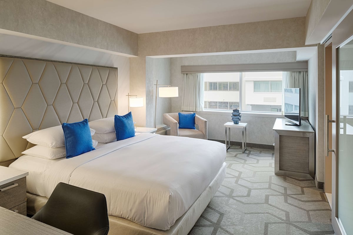 A hotel room with a large bed, a desk, a chair, a small table, and a window with curtains.