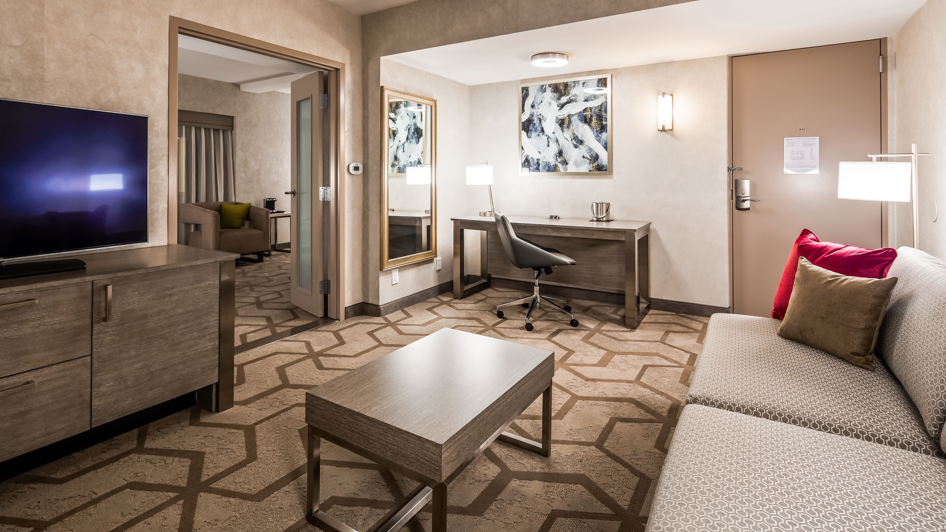 A hotel room with a TV, a desk, a chair, a sofa, and a patterned carpet.