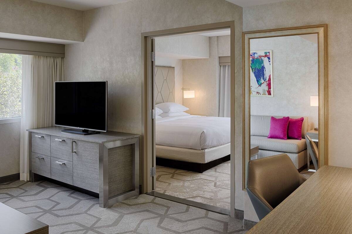 A hotel room with a bed, a TV on a cabinet, a desk, and a sofa.