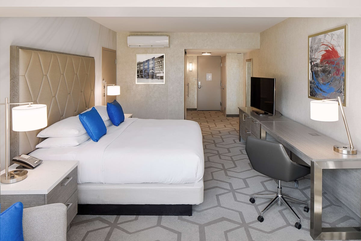 A hotel room with a large bed, a desk, a chair, a TV, and a painting on the wall.