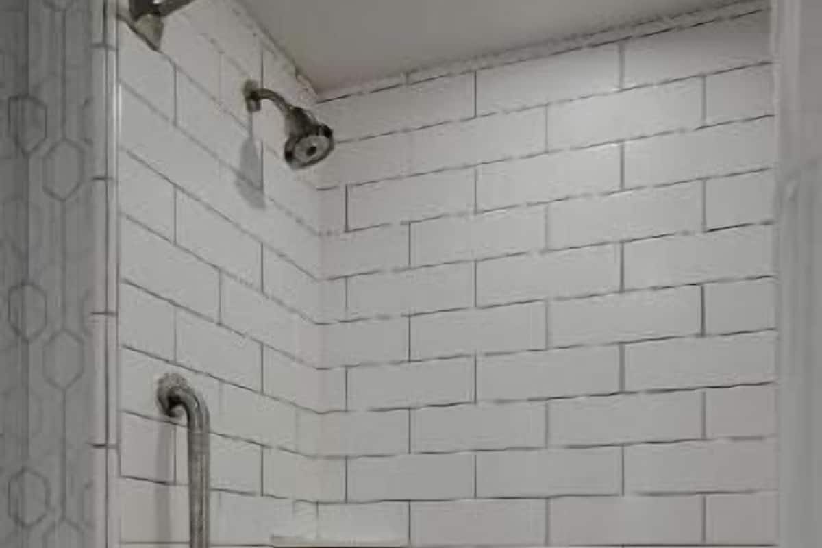 A bathroom with white tiled walls, a white bathtub, and a shower area with a grab bar.