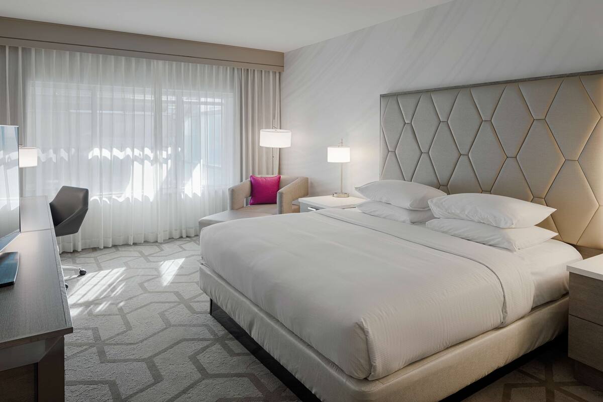 A hotel room with a large bed, a desk, a chair, and a nightstand.