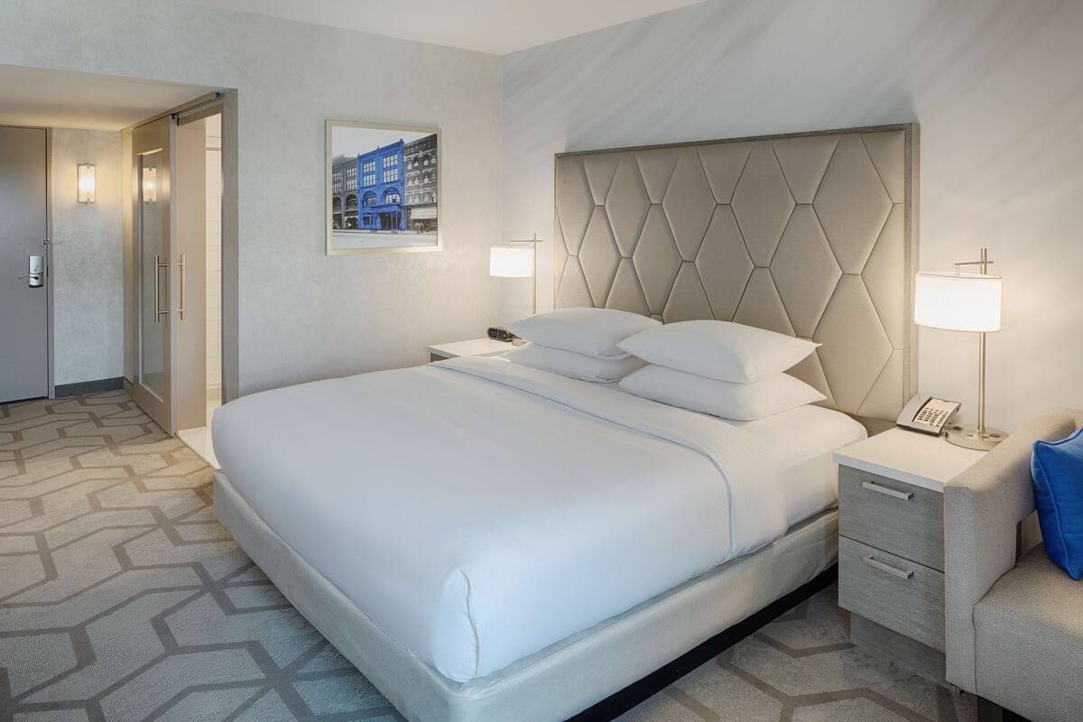 A hotel room with a large bed, a bedside table with a lamp, and a framed picture on the wall.