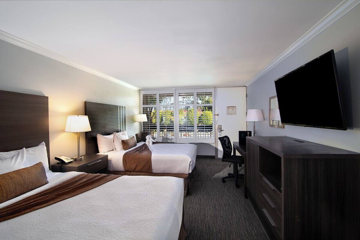 A hotel room with two beds, a TV, a desk, and a view of the outdoors.