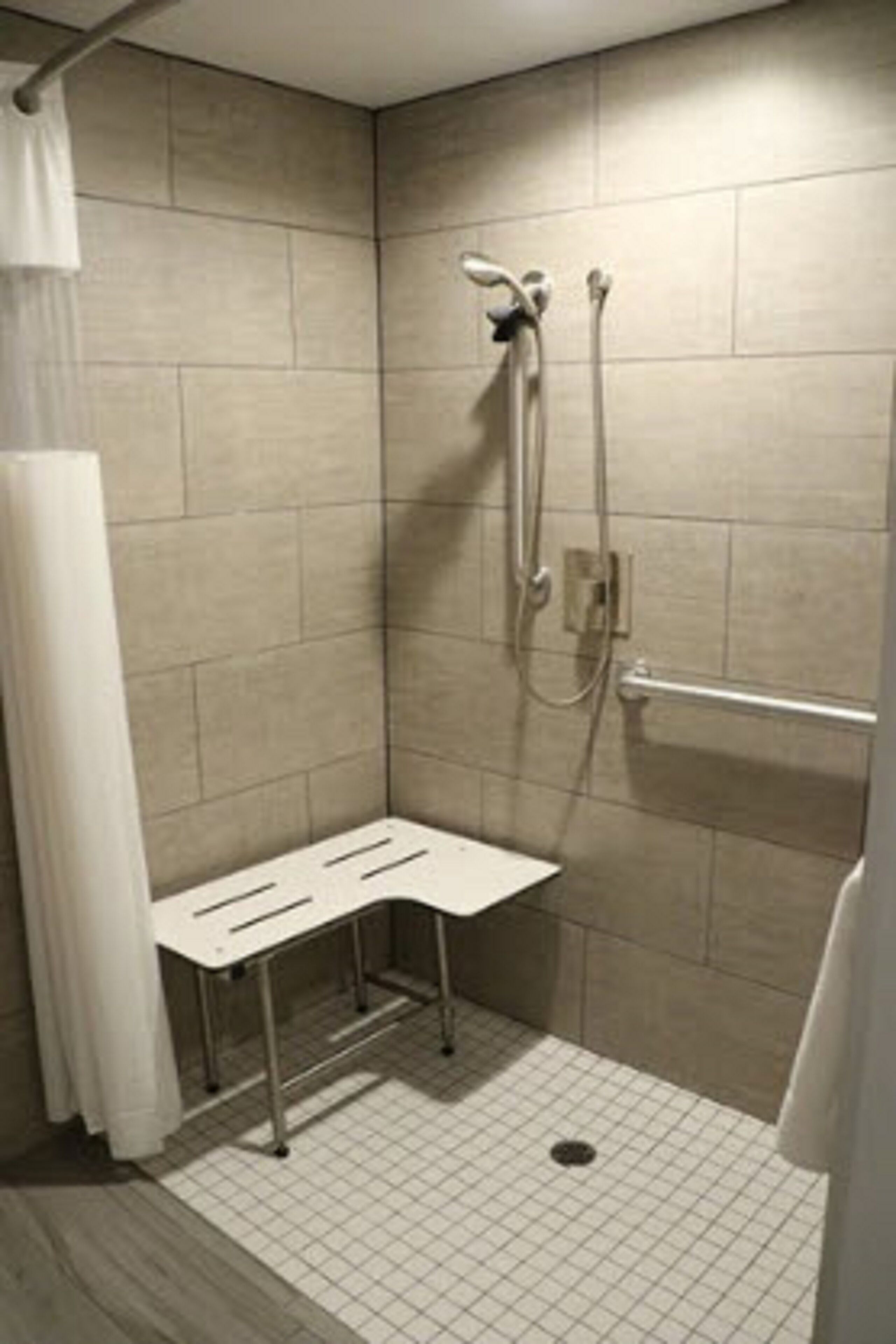 A small, enclosed shower area with a white bench, tiled walls, and a showerhead.