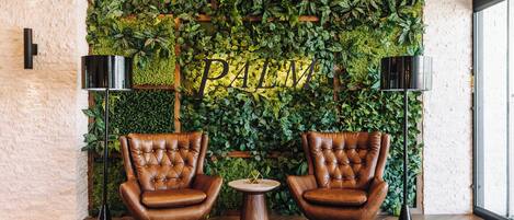 A room with two leather armchairs, a small wooden table, and a wall covered in green foliage with the word "PALM" visible.