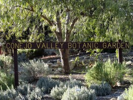 En skylt för Conejo Valley botaniska trädgård, omgiven av olika växter och träd.