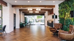 A spacious lobby with wooden flooring, leather armchairs, a reception desk, and a green wall with plants. - Palm Garden Hotel (Thousand Oaks)