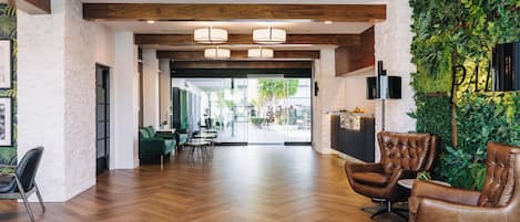 Un hall d’entrée spacieux doté d’un plancher en bois, de fauteuils en cuir, d’un comptoir d’accueil et d’un mur végétal.